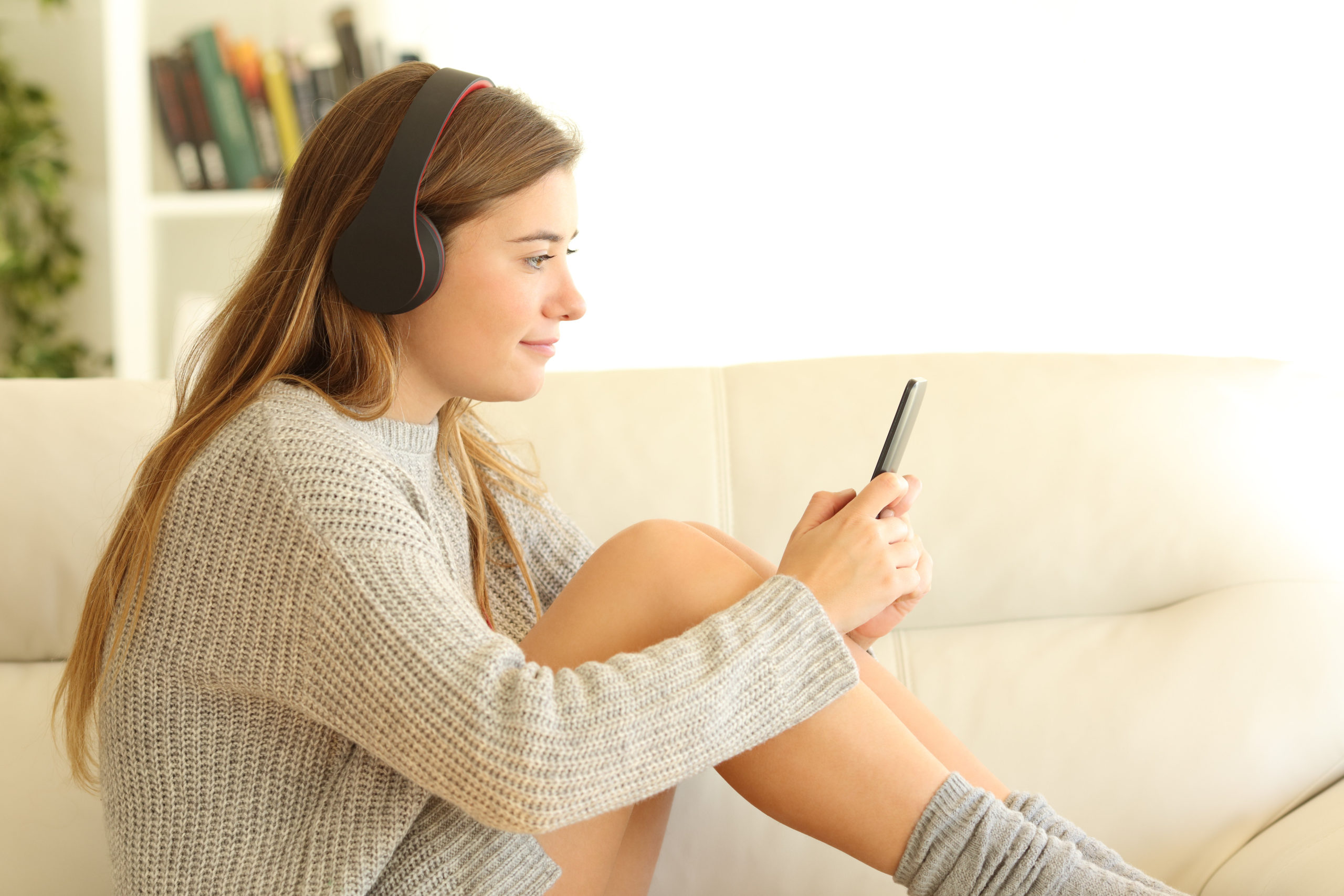 Side view portrait of a teen listening to music sitting on a sofa in the living room in a house