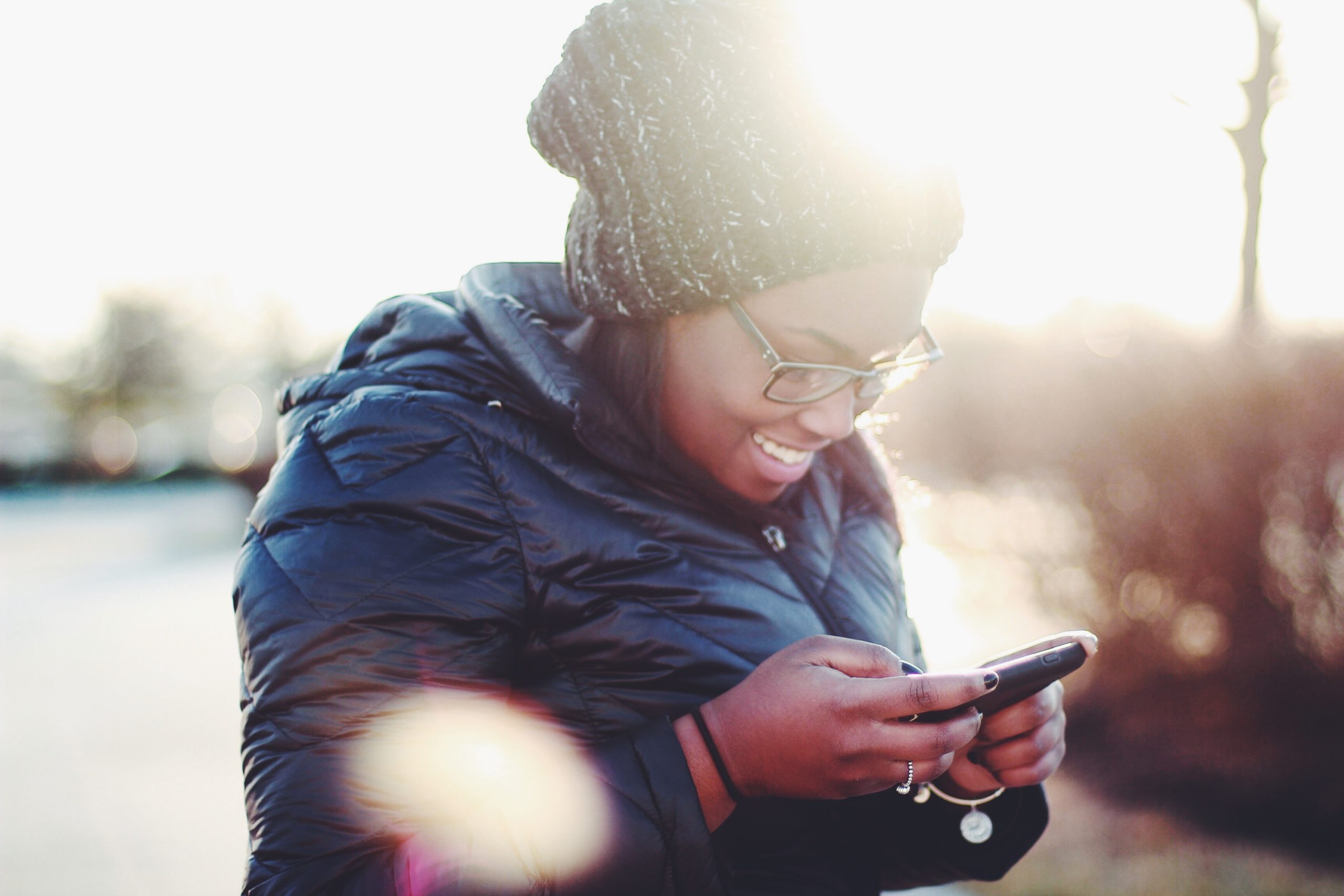 smiling woman wearing black coat using smartphone