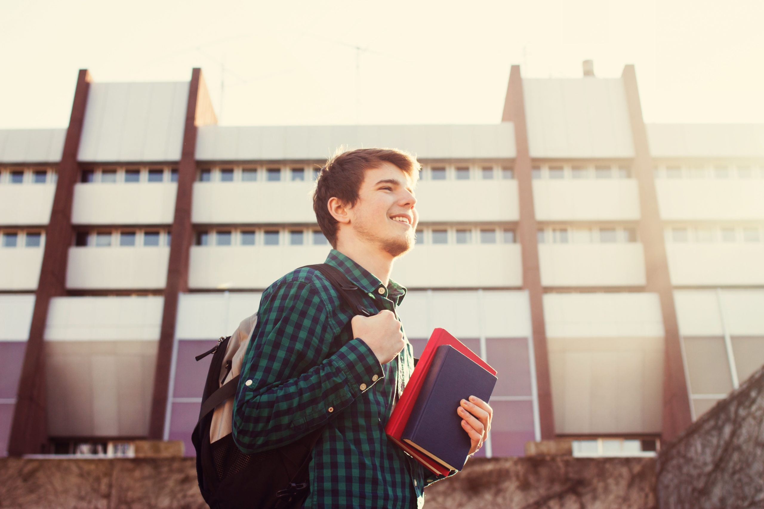 male student holding a book and a bag on a university campus